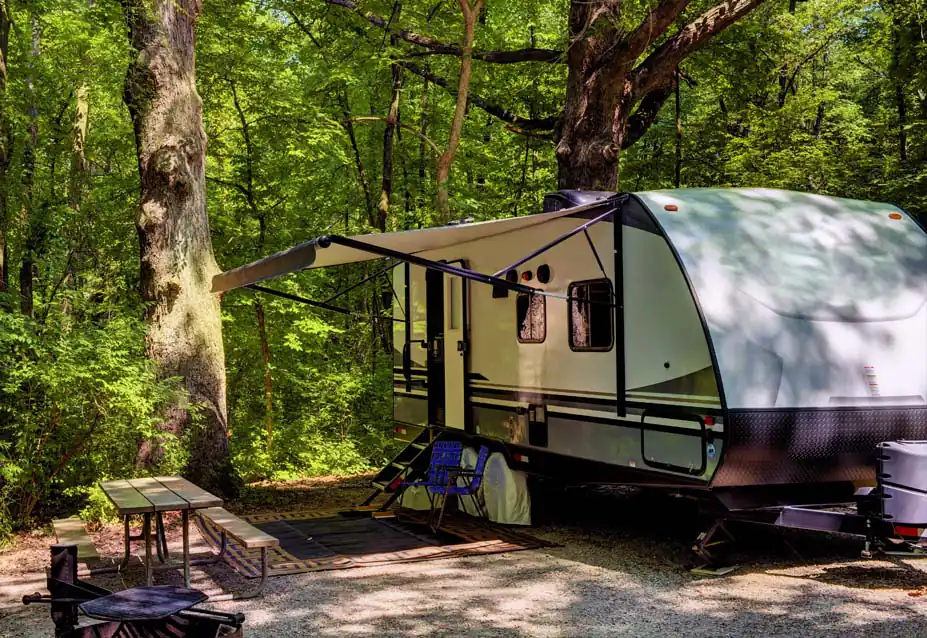 Travel trailer with its awning out at a shaded forest campsite